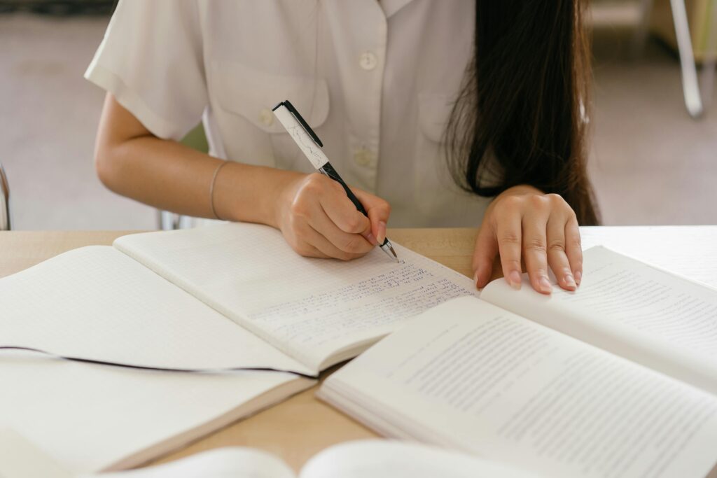 Woman writing notes in a notebook, focusing on study. Hands visible close-up.