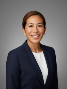 Mau Lingua 代表・講師|マヤ(Maya) 洗練されたモダンオフィスで、ネイビージャケットと白いインナーを着用し、笑顔で正面を向いて立つ日本人女性講師(マヤ)のプロフィール写真(腰から上のアングル)